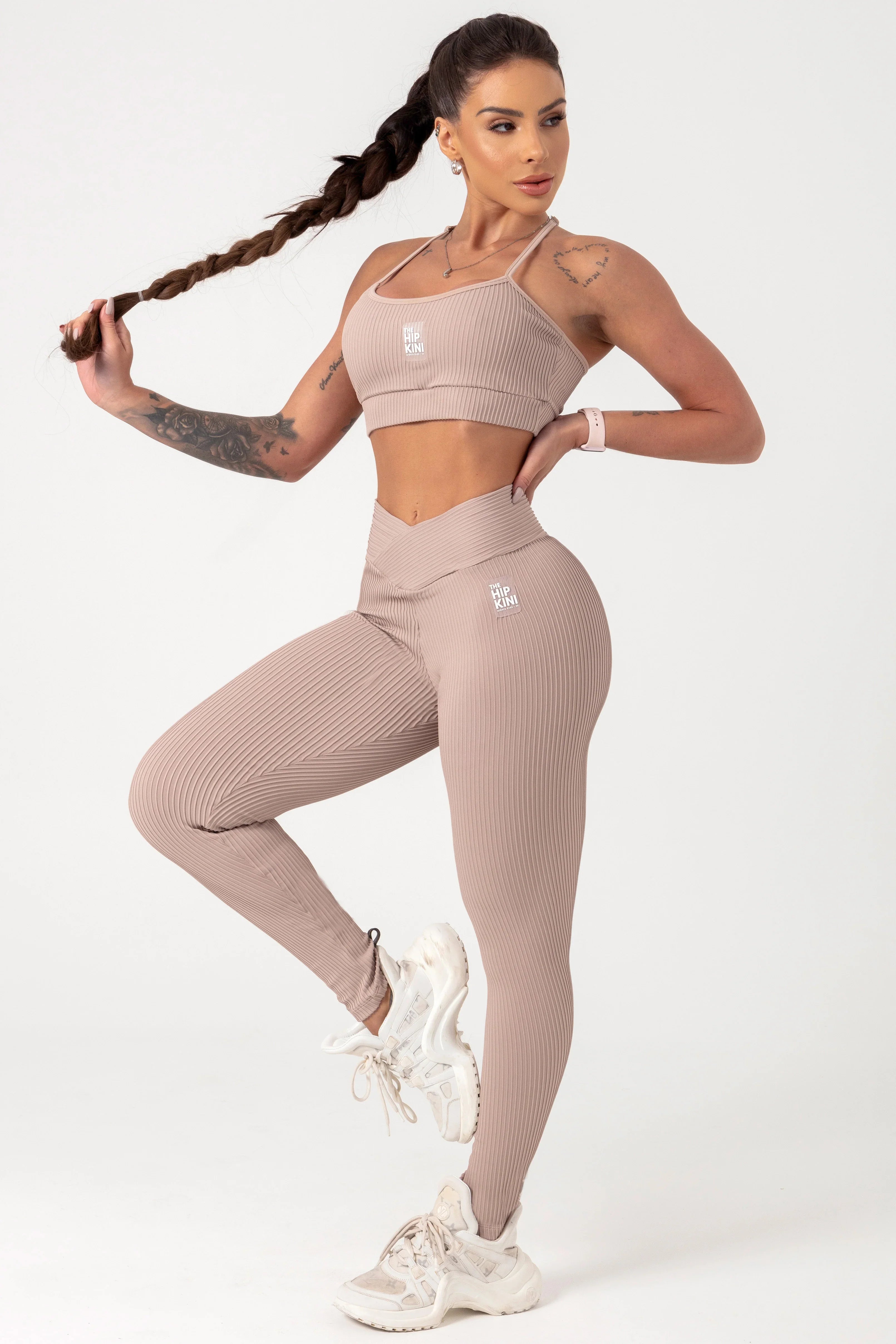 girl wearing tan bra top and legging posing on 1 leg and the other elevated.