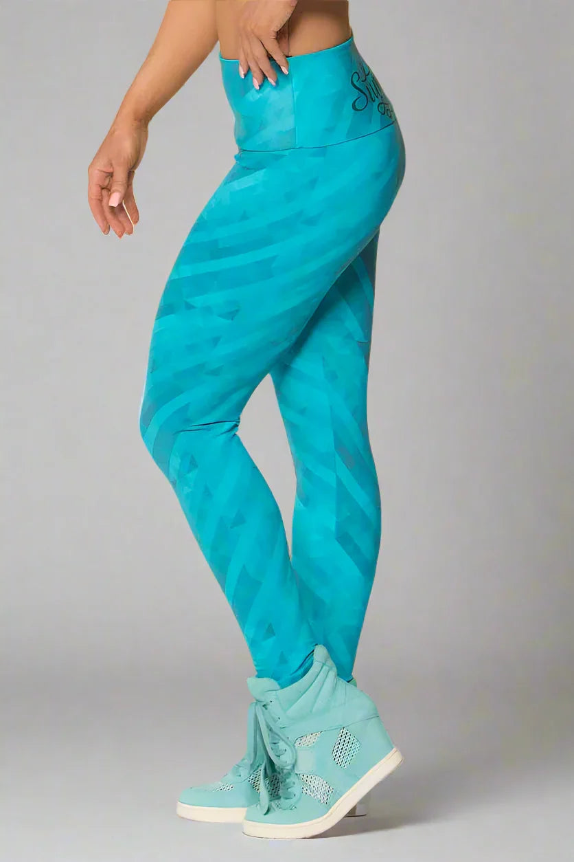 A side view of a person wearing Alto Giro Pacific Shadow Legging in turquoise color with a shadow line design and a fun applique of summer on the back.