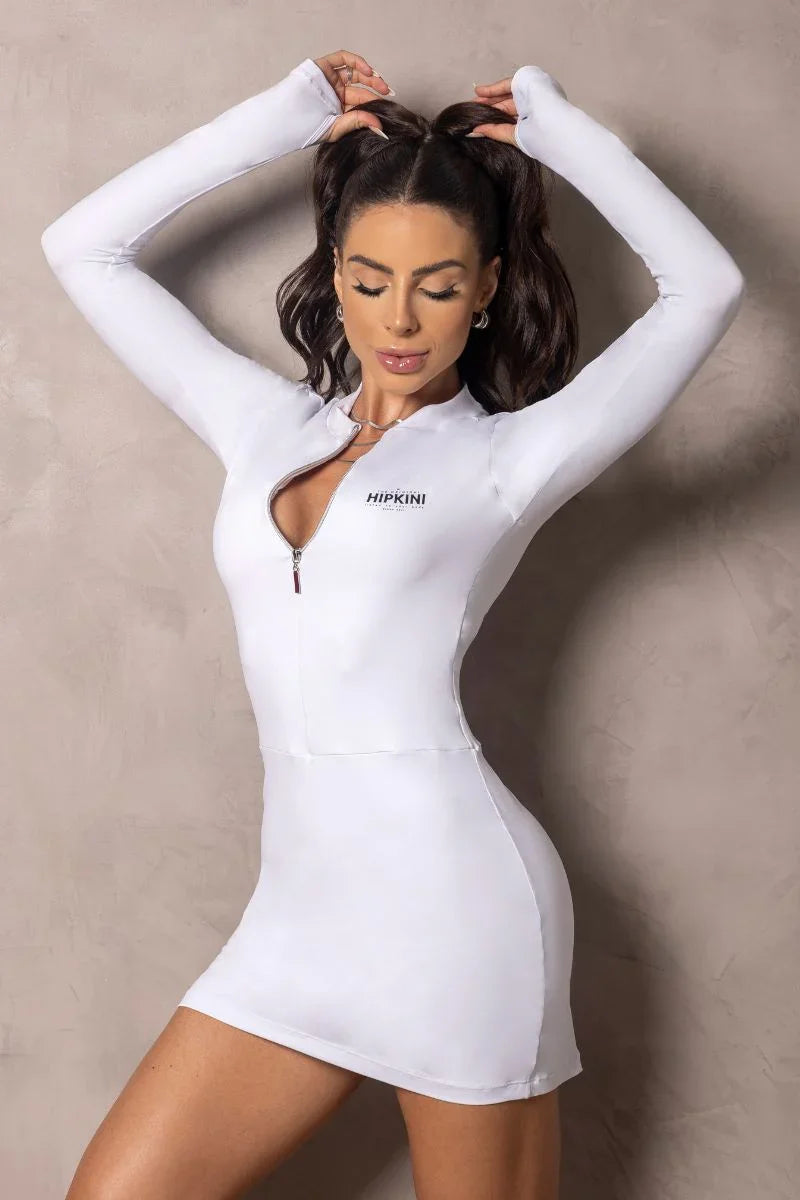 Woman in a white outfit with a logo on a neutral background arms over head