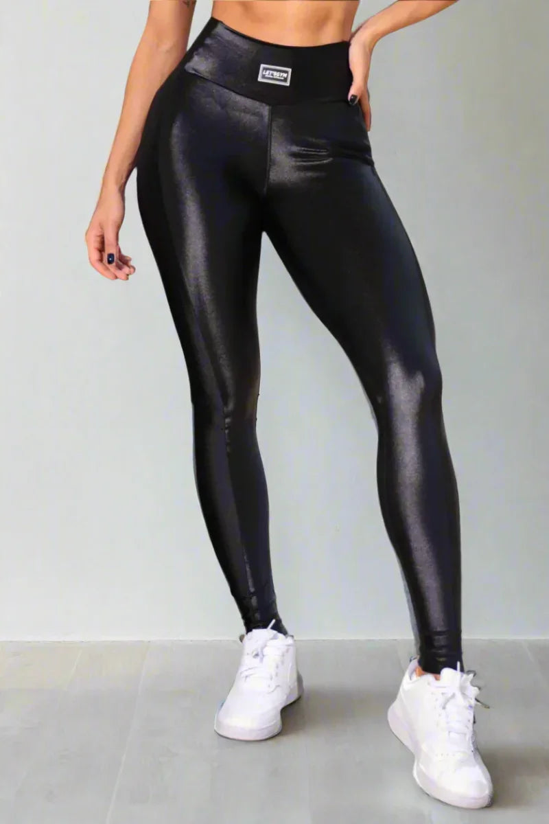 A model wearing high-waisted black gym leggings with a sheen finish and a wide waistband, paired with white sneakers.