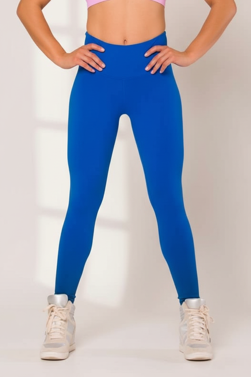 A person wearing a blue legging with a wide waist, paired with a white top and shoes, standing in front of a mirror.