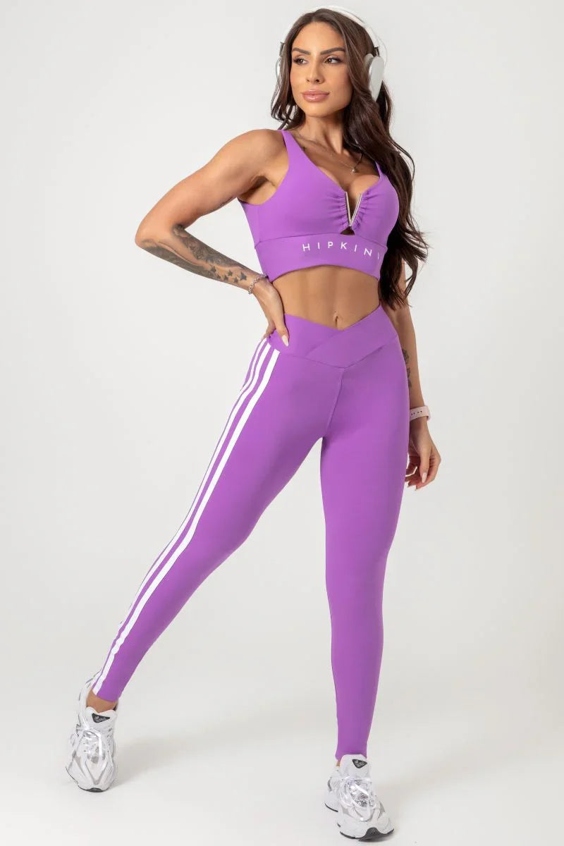 A person wearing a purple Hipkini Victory V Front Legging with white side striping, paired with a white top and white sneakers.